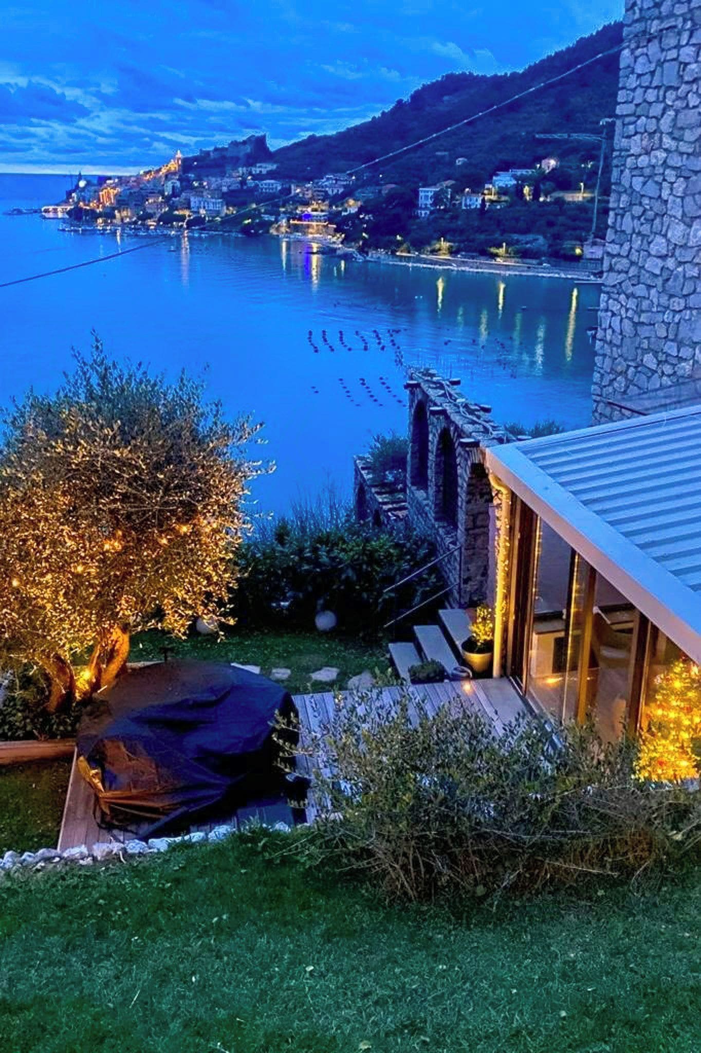 A lakeside property with a stone building, a wooden deck, and a view of the lake and distant town.