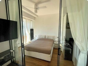 A bedroom with a bed, a television, a ceiling fan, and a window with curtains. - Private sea-view garden near Portovenere (Portovenere)