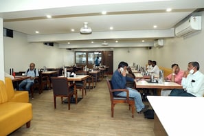 Sala de conferências com várias mesas e cadeiras, equipada com microfones e laptops, indicando um ambiente para reuniões ou seminários.