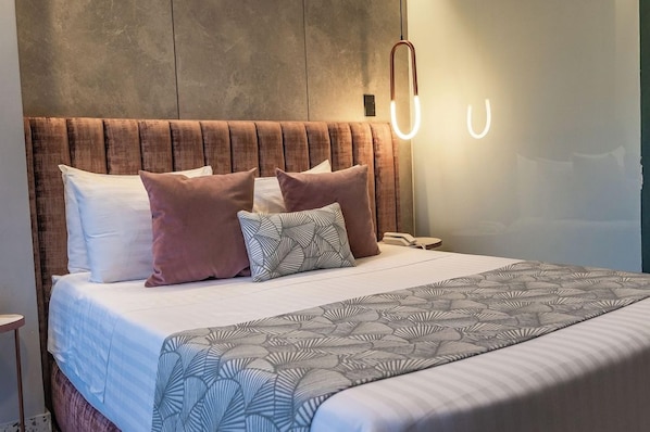 A neatly made bed with a patterned bedspread, a headboard with a textured design, and a bedside lamp. - Glow Medellín (Medellín)