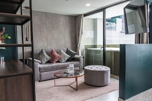 A modern living room with a grey sofa, a glass coffee table, and a round ottoman. - Glow Medellín (Medellín)