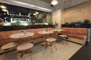A bar area with round tables and cushioned seating, a brick wall, and a tiled floor. - Glow Medellín (Medellín)