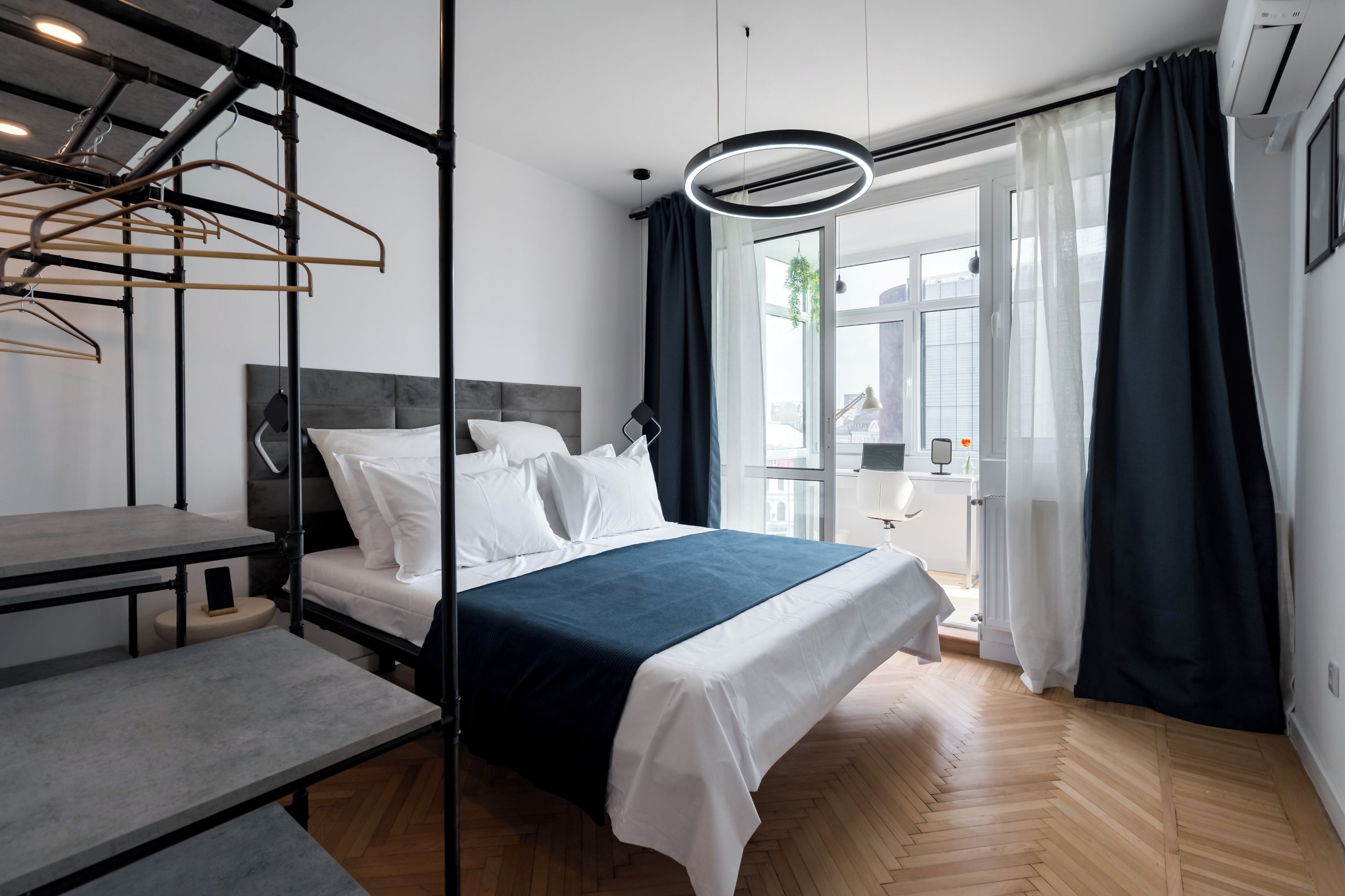 A modern bedroom with a bed, a desk, and a hanging clothes rack.