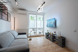 A modern living room with a grey sofa, a TV mounted on the wall, and a herringbone wooden floor. - AviStay Bratianu Old Town (București)