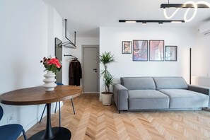 Una sala de estar moderna con un sofá gris, una mesa de comedor de madera con un florero y una planta en maceta.