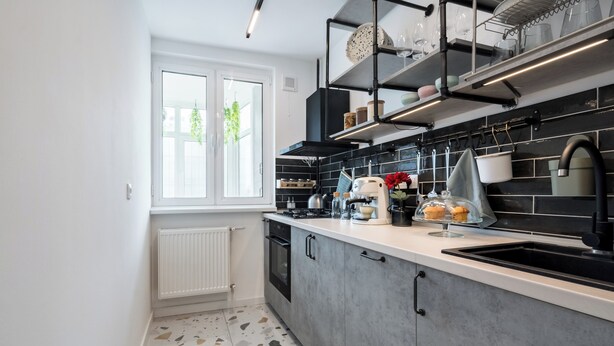 A modern kitchen with a white countertop, black backsplash, and a window with a view of greenery. - AviStay Bratianu Old Town (București)