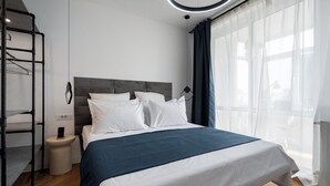 A modern bedroom with a bed, a nightstand, a hanging light fixture, and a window with sheer curtains. - AviStay Bratianu Old Town (București)