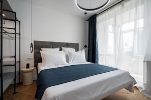 A modern bedroom with a bed, a nightstand, a hanging light fixture, and a window with sheer curtains. - AviStay Bratianu Old Town (București)
