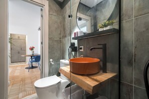Un baño moderno con cabina de ducha de vidrio, tocador de madera y un inodoro blanco.