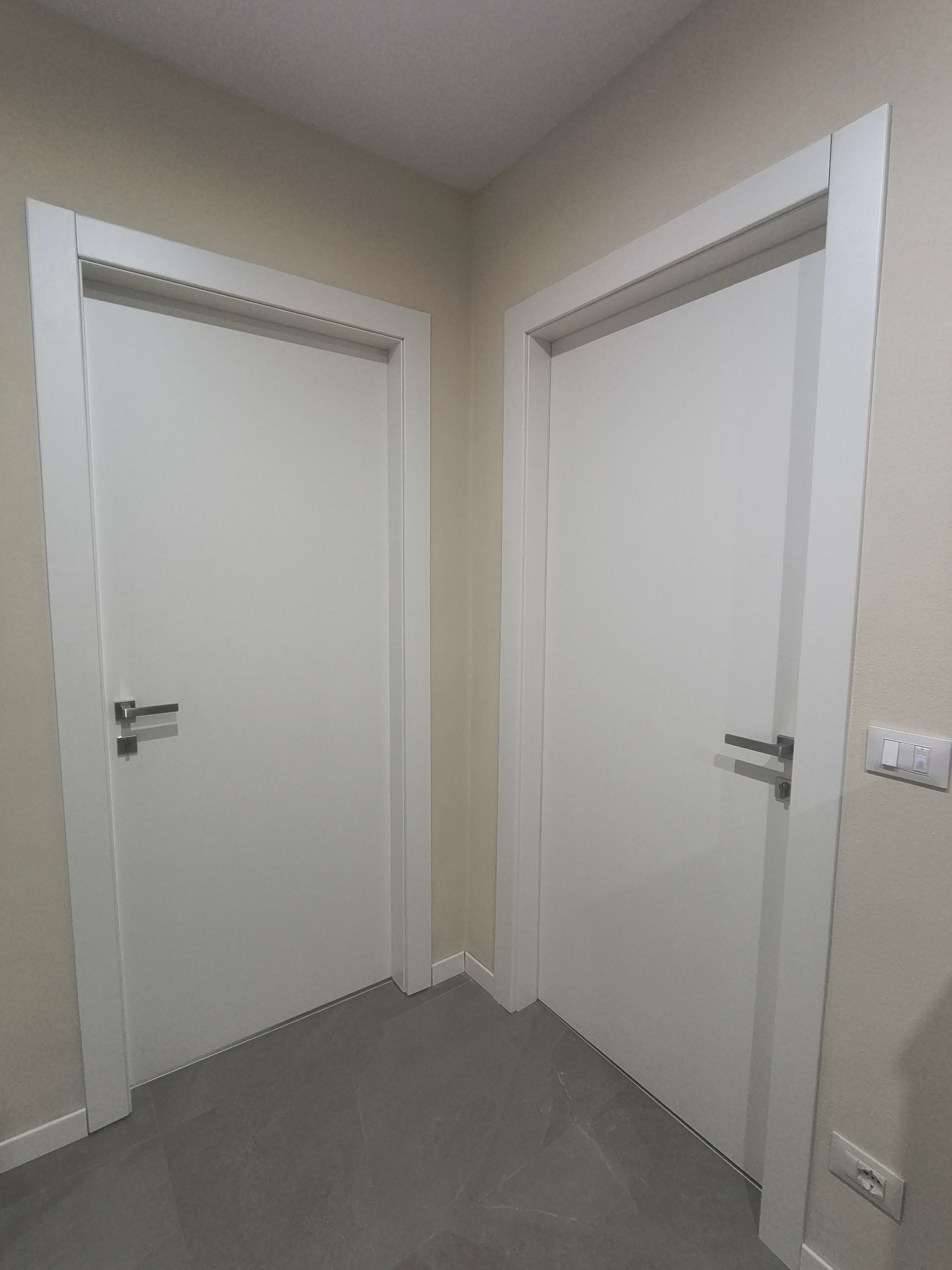 A hallway with two white doors, a light switch, and a wall socket.