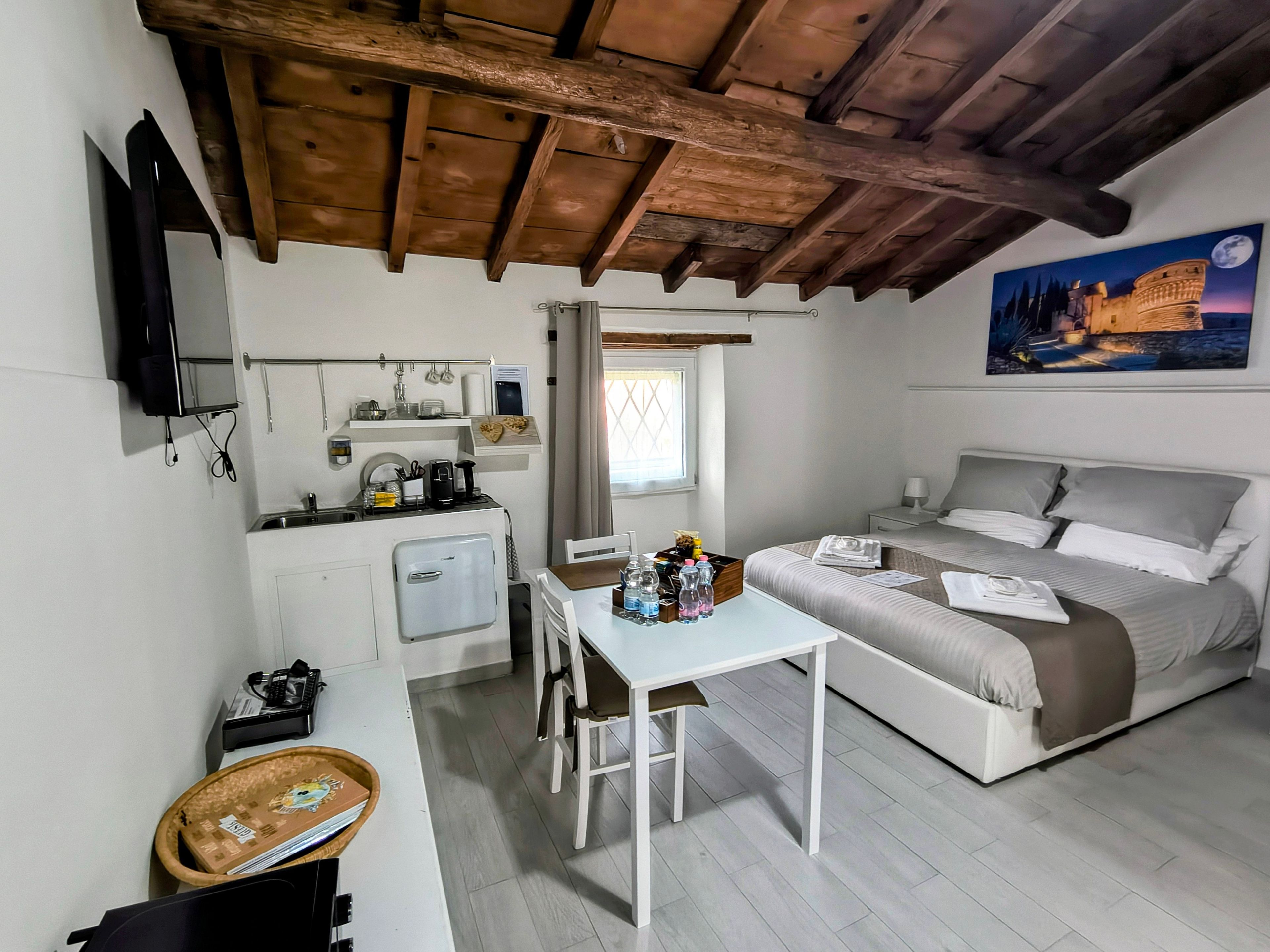 Habitación de hotel compacta con kitchenette, cama, mesa de comedor y un cuadro de un castillo.