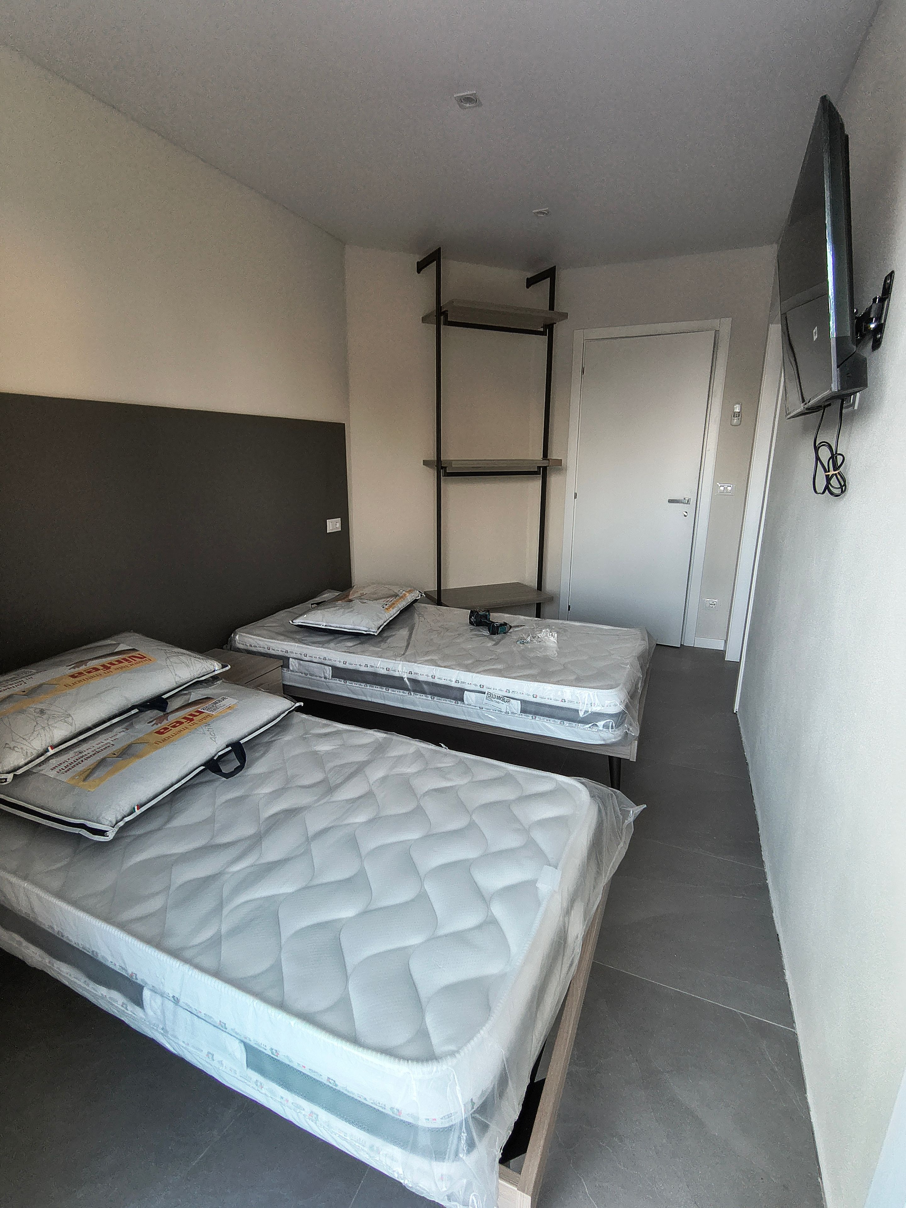 Ein Zimmer mit zwei Matratzen, einem an der Wand befestigten Fernseher und einer Tür.