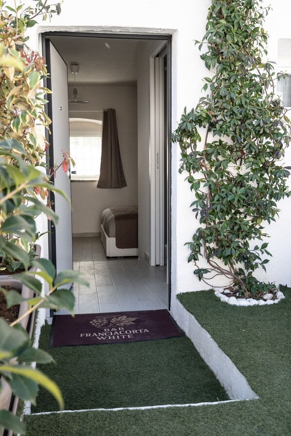 A doorway leading to a room with a bed, a hanging light fixture, and a potted plant.