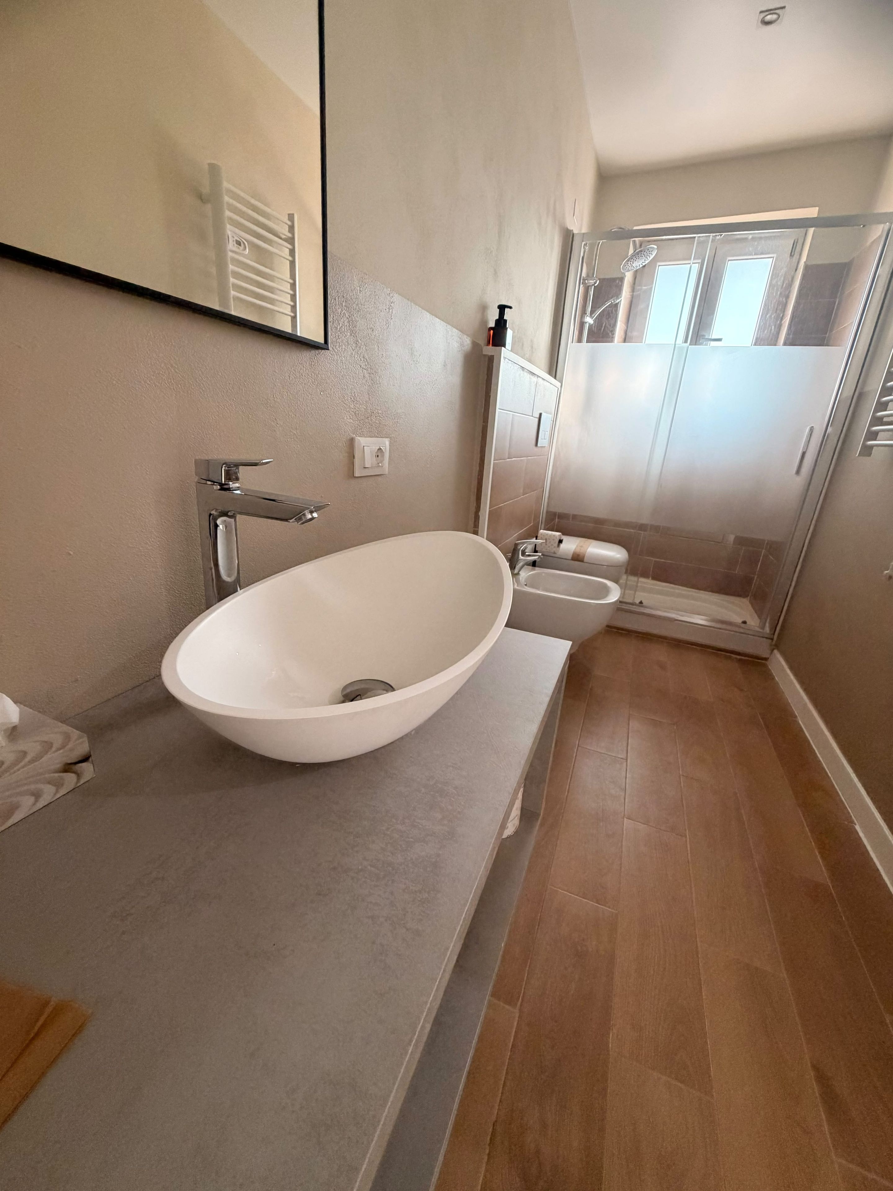 Ein Badezimmer mit einem großen weißen Waschbecken, einem Spiegel, einer Toilette und einer Duschkabine.