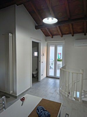 A room with a white radiator, a white door leading to a bathroom, a white staircase, and a table with a pair of scissors on it.