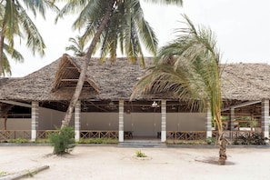 Un edificio frente a la playa con techo de paja, asientos al aire libre y palmeras.