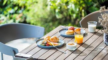 A wooden table with breakfast items including croissants, a glass of orange juice, and a plate of food.