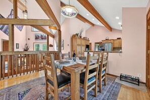 Ein geräumiger Essbereich mit Holzböcken und einem für eine Mahlzeit gedecktem Tisch, eine Küche mit Holzschränken und modernen Geräten sowie eine hohe Decke mit freiliegenden Holzbalken.