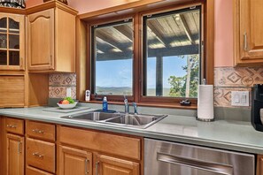 Eine Küche mit Holzausstattung, einem Edelstahlspülbecken, einem Fenster mit Ausblick und einer Arbeitsplatte mit Obstschale.