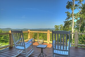 Eine Holzterrasse mit zwei Schaukelstühlen und einem kleinen Tisch, mit Blick auf eine gebirgige Landschaft.
