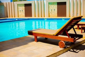 Un área junto a la piscina con una silla de descanso y un suelo de baldosas.