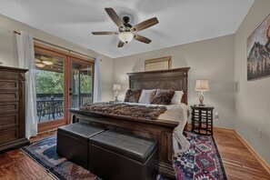 A bedroom with a large bed, a ceiling fan, a nightstand with lamps, and a view through a glass door to an outdoor patio. - Big Mountain view cabin rental in Walnut Mountain. Pet Friendly, hot tub and pool table (Ellijay)