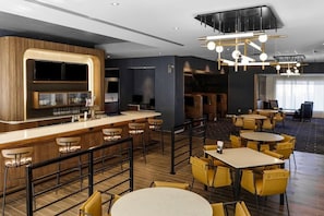 A modern bar area with a counter, stools, and a seating area with tables and chairs. - Courtyard by Marriott Madison (Madison)