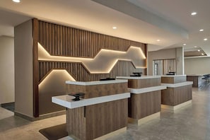 A reception area with a modern design, featuring a wooden reception desk and a wall with a geometric light pattern. - Courtyard by Marriott Madison (Madison)