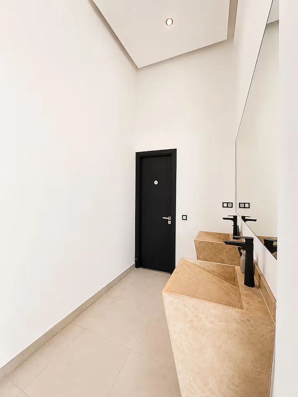 Une salle de bain moderne avec un grand miroir, une porte noire et des carreaux de couleur beige.