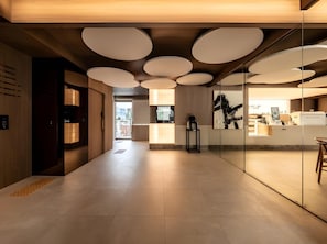 Un interior moderno con un espacio central abierto, una zona de recepción con separadores de vidrio y un techo con luminarias circulares.