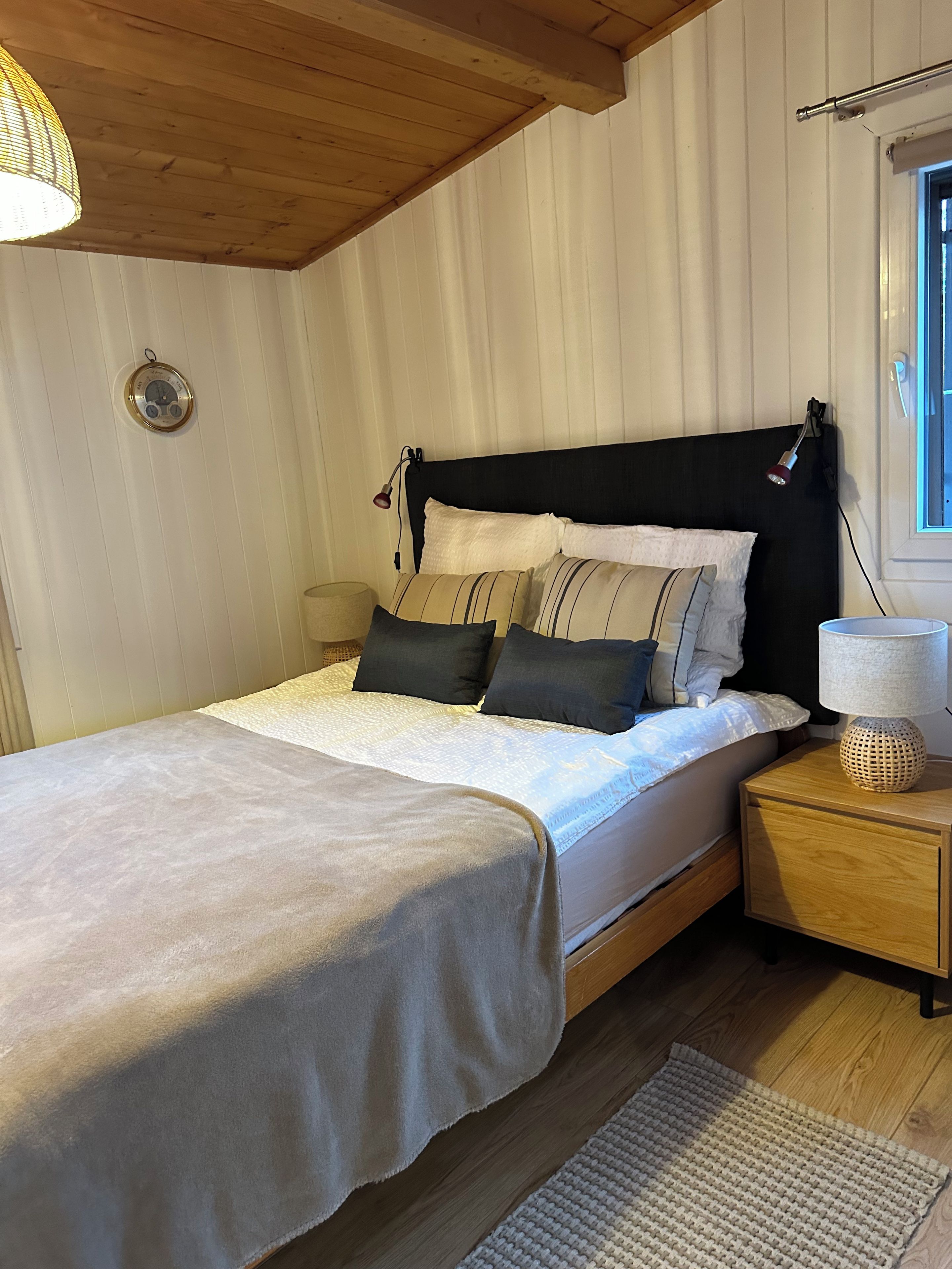 Un lit bien fait, avec une tête de lit, une lampe de chevet et une horloge murale.