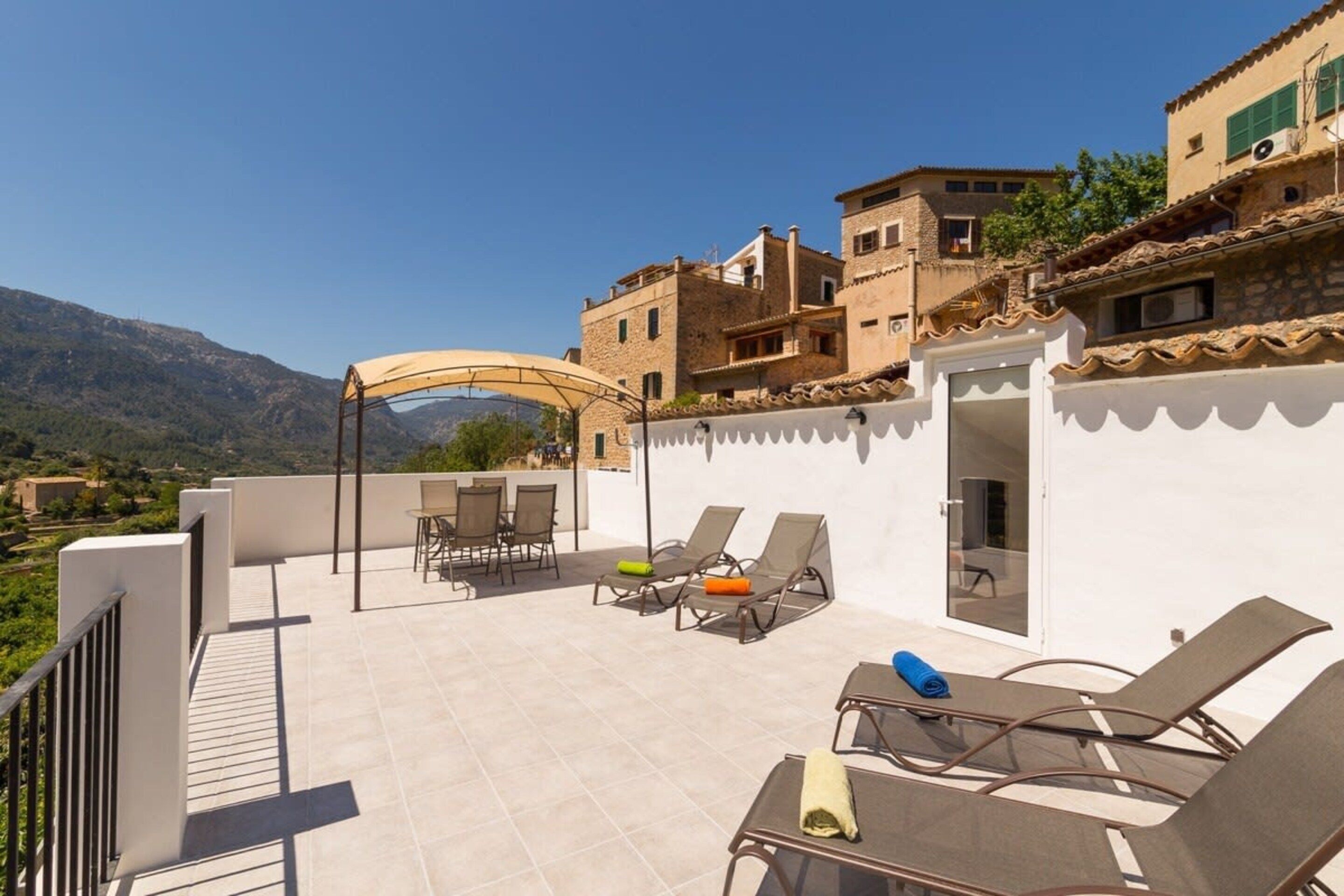 A rooftop terrace with outdoor seating, a covered area, and a view of the surrounding landscape.