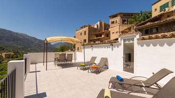 A rooftop terrace with outdoor seating, a covered area, and a view of the surrounding landscape.