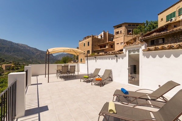 Una terraza en la azotea con mobiliario exterior, una zona techada y vistas del paisaje circundante.