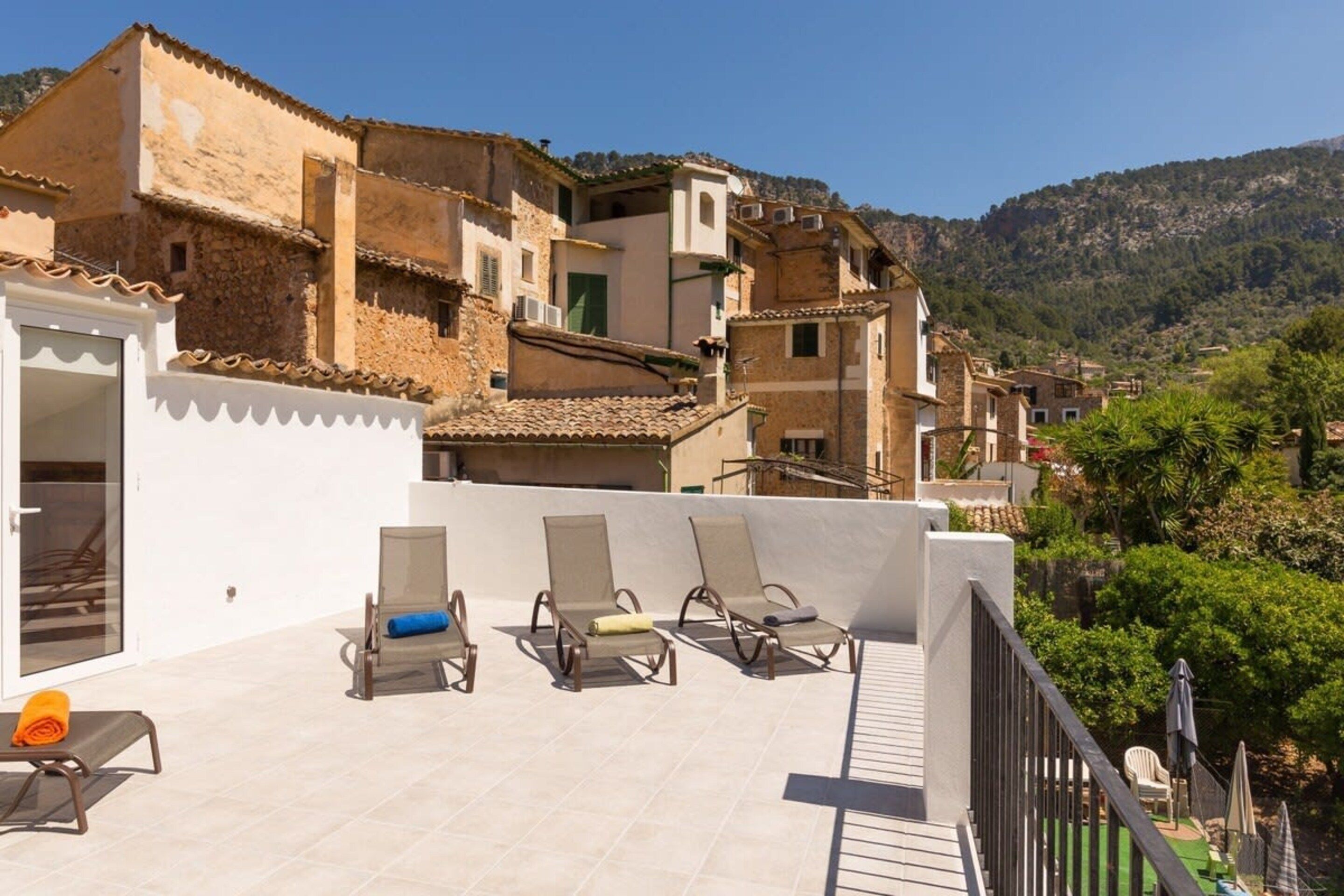 A rooftop terrace with lounge chairs and a view of a hillside village.