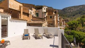 A rooftop terrace with lounge chairs and a view of a hillside village.
