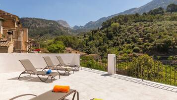 A terrace with lounge chairs and a view of a mountainous landscape.