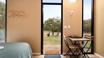 A bedroom with a bed, a wooden table, and a view of an outdoor area with a barbecue and chairs.