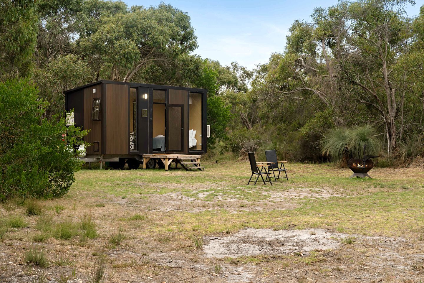 A mobile home with a deck, two chairs, and a barbecue grill in a natural setting.