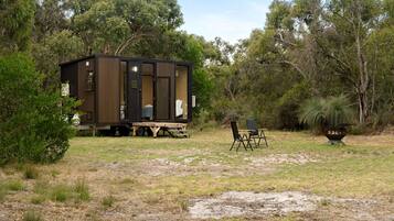 A mobile home with a deck, two chairs, and a barbecue grill in a natural setting.
