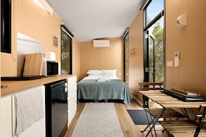A compact room with a bed, a small kitchenette, a dining table, and a bench.