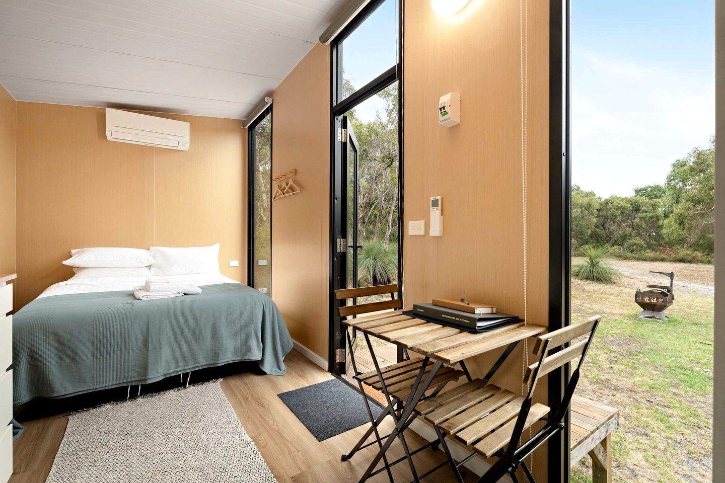 Ein Schlafzimmer mit einem Bett, einem Schreibtisch mit Stuhl und Blick ins Freie.