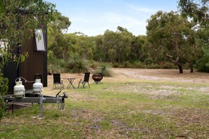 Un espace extérieur rustique doté d’une structure en bois, de deux bouteilles de gaz, d’un barbecue et de mobilier d’extérieur.