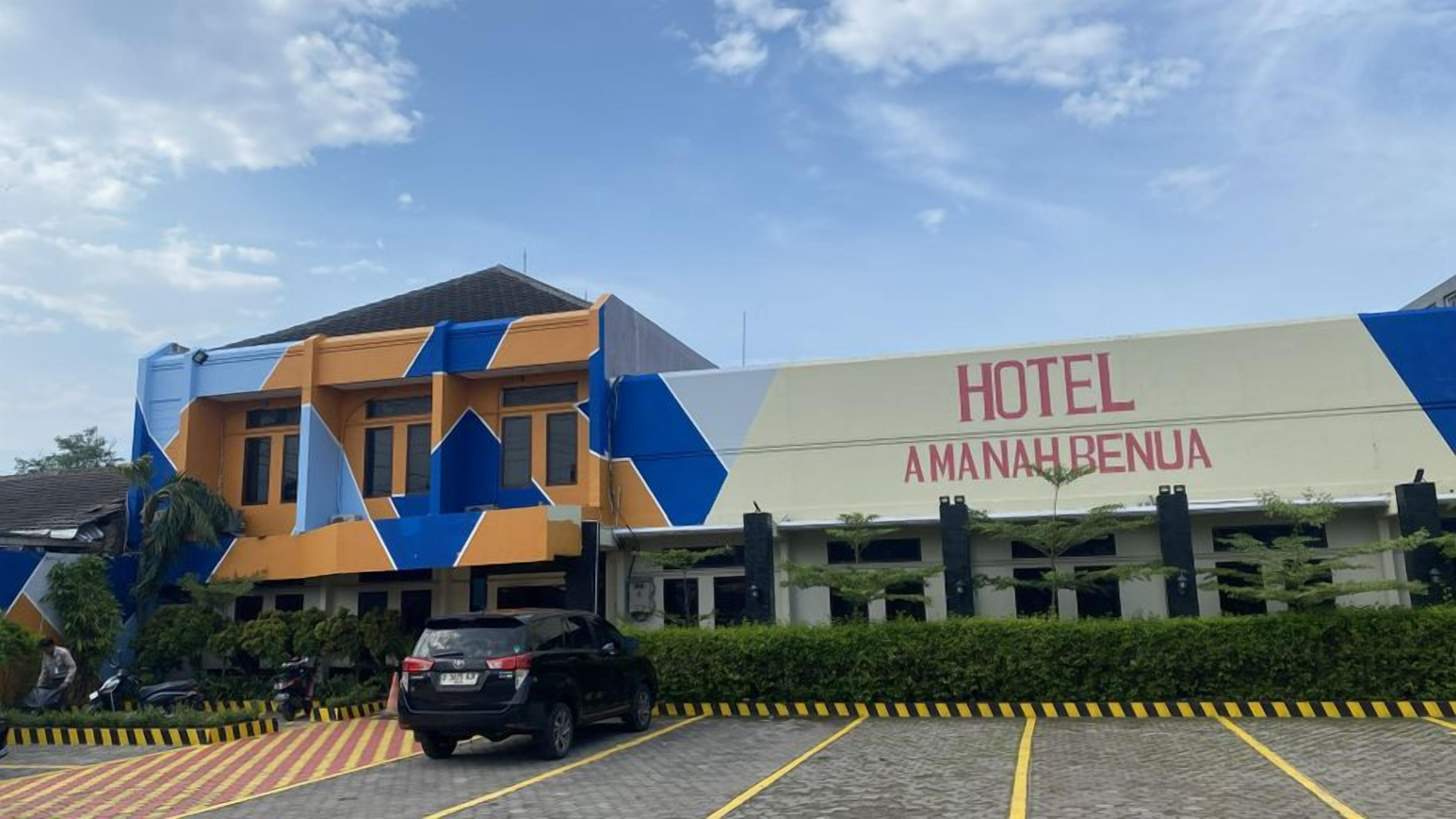 A hotel with a modern facade, a parking area, and a clear sky.