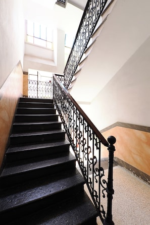 A staircase with ornate black railings and a marble wall. - Contempora - Cozy, Designer Two-Room Apartment for 2 | Monumentale & Sarpi M5 (Milano)