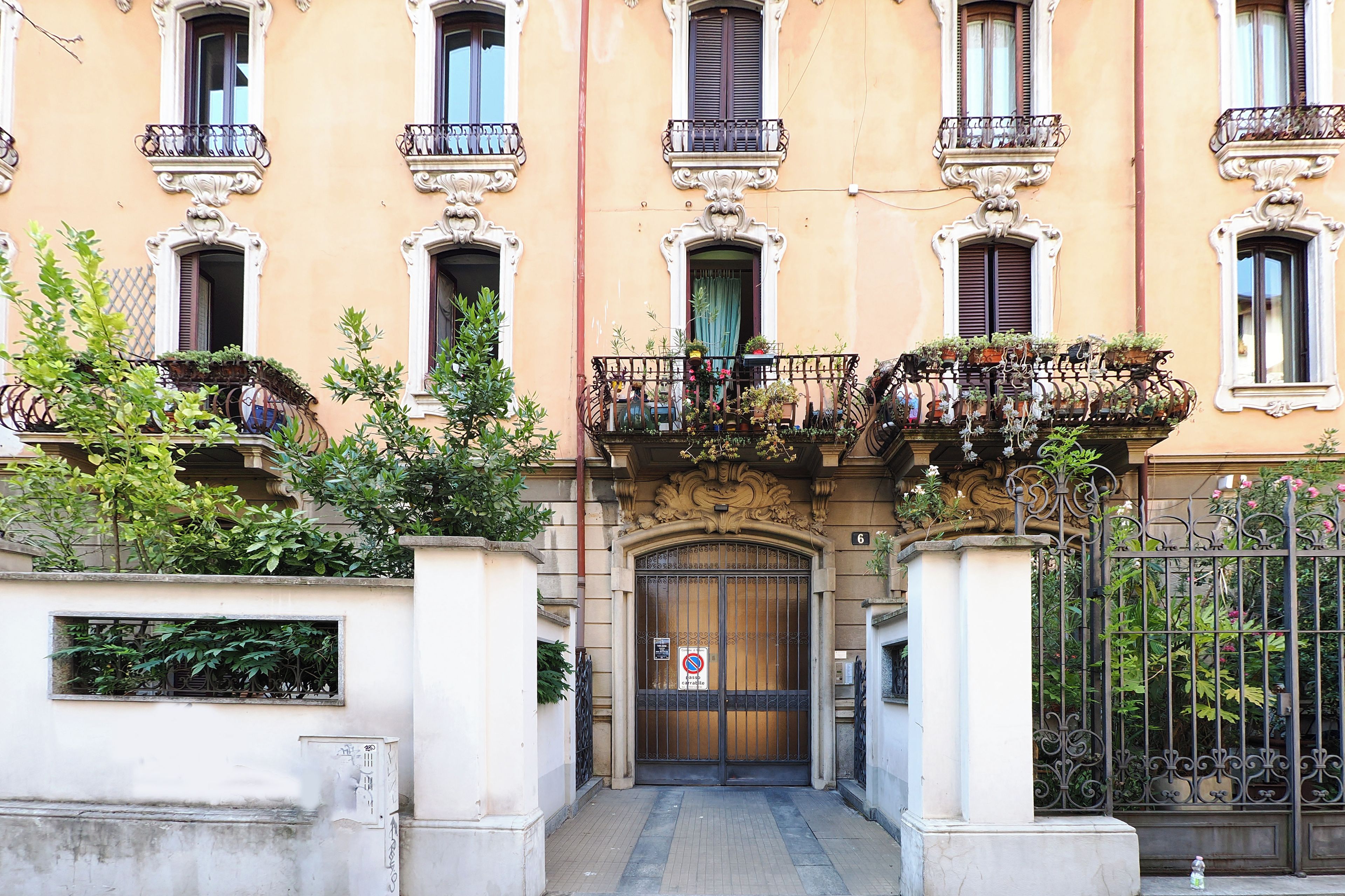 Un edificio con entrada central, varios balcones con plantas y acceso mediante portón.