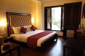 Une chambre d’hôtel avec un grand lit, une table de chevet, un bureau et une fenêtre avec des stores.