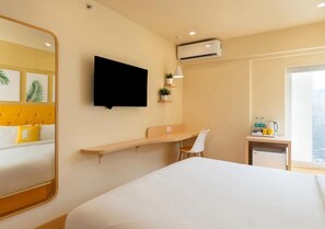 A hotel room with a bed, a desk with a chair, a TV mounted on the wall, and an air conditioning unit. - Bloom Hotel - Saki Vihar Powai (Mumbai)