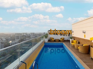 A rooftop pool with a city view, a 'bloom' sign, and yellow chairs. - Bloom Hotel - Saki Vihar Powai (Mumbai)
