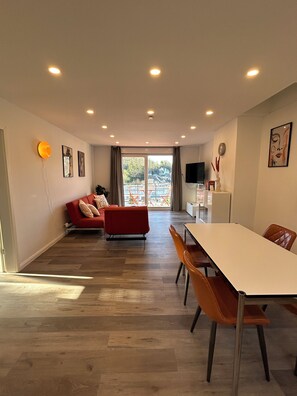 A modern living room with a red sofa, a dining table with chairs, and a large window with a view of a building.